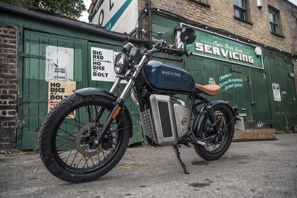 A Maeving electric motorcycle is parked in front of a building that says servicing.