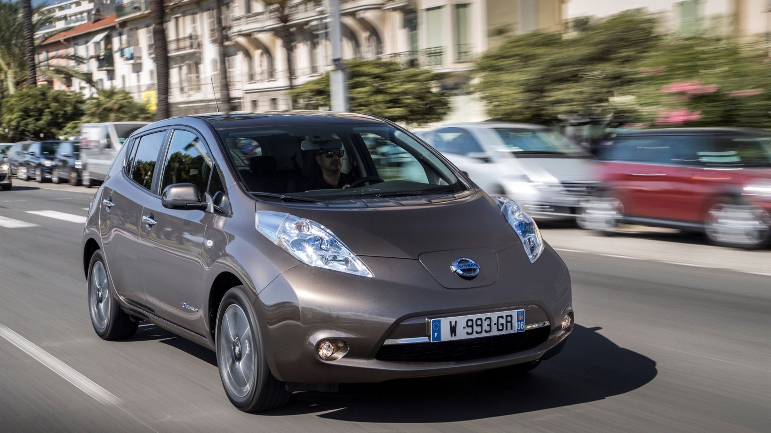 A  Nissan leaf electric car is driving down a city street.