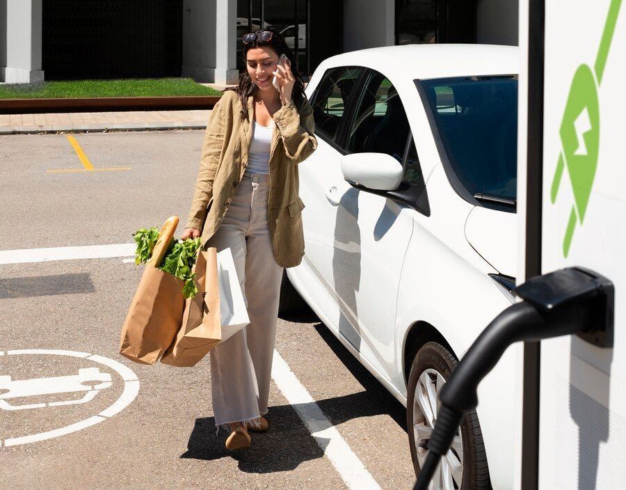 A woman is talking on a cell phone while charging her electric car.