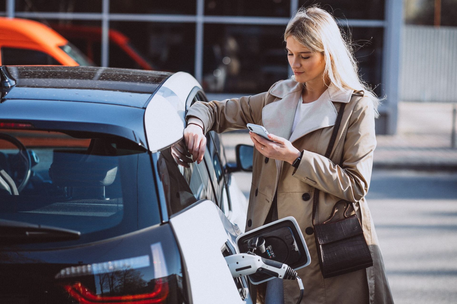 A woman is charging her electric car while looking at her phone.