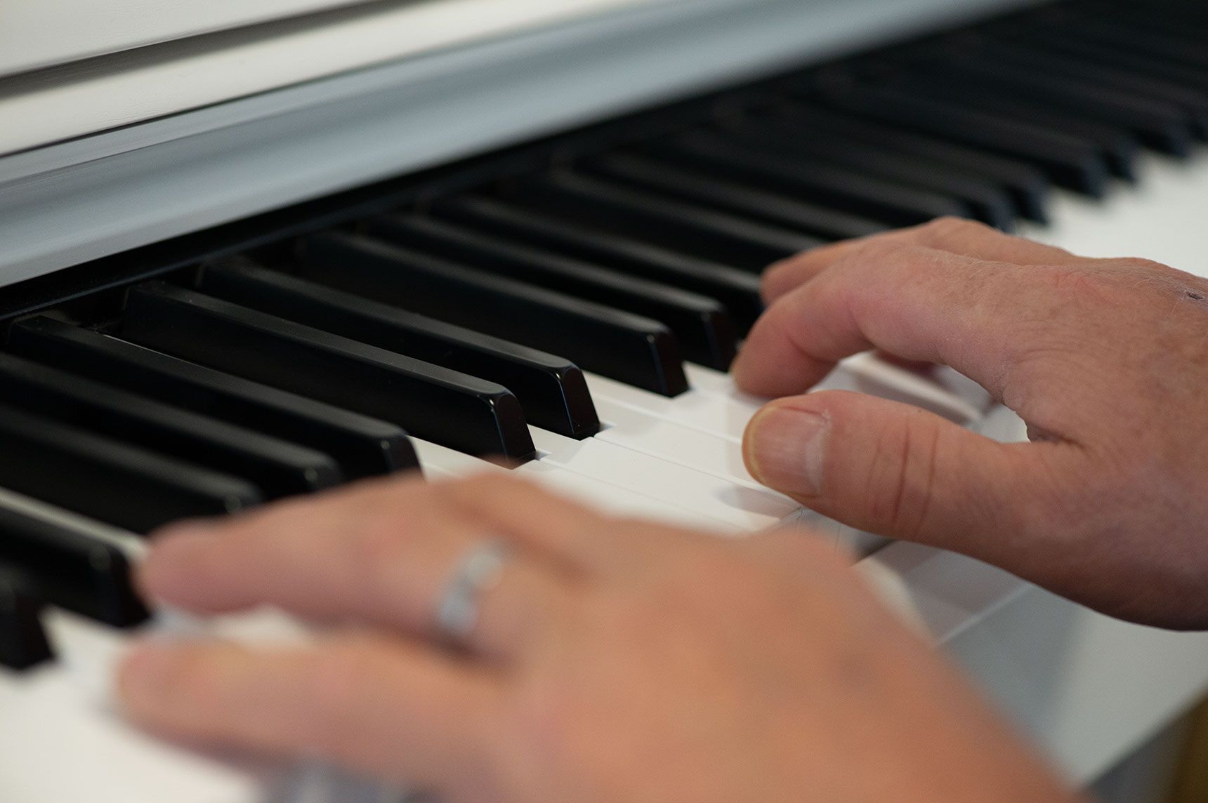 Hände, die ein weisses Klavier spielen, Finger auf den schwarzen und weissen Tasten, ein Ring an einem Finger.