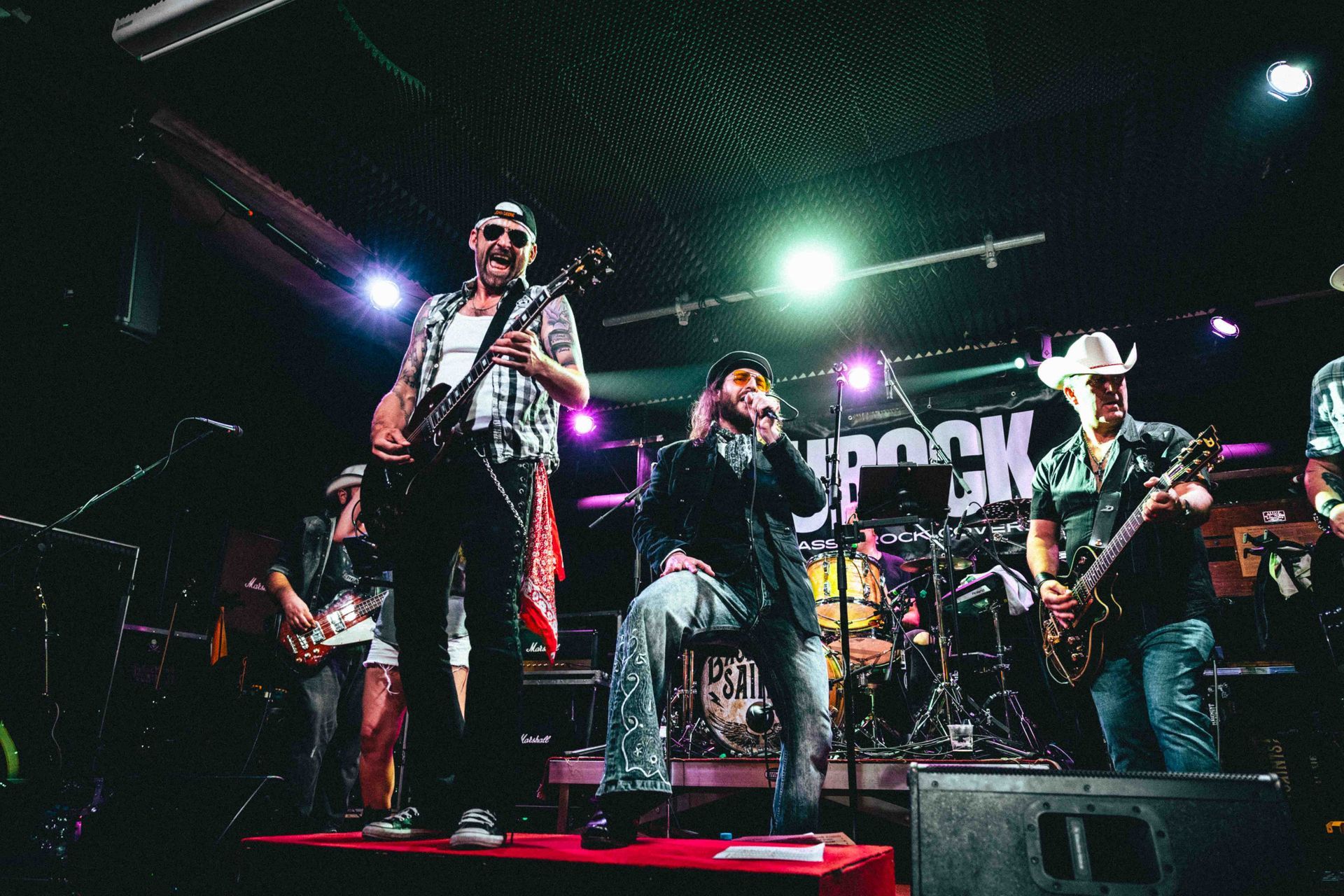 Zwei Männer spielen in einem Studio E-Gitarre; einer mit Bart, lächelnd, der andere mit Tätowierung.