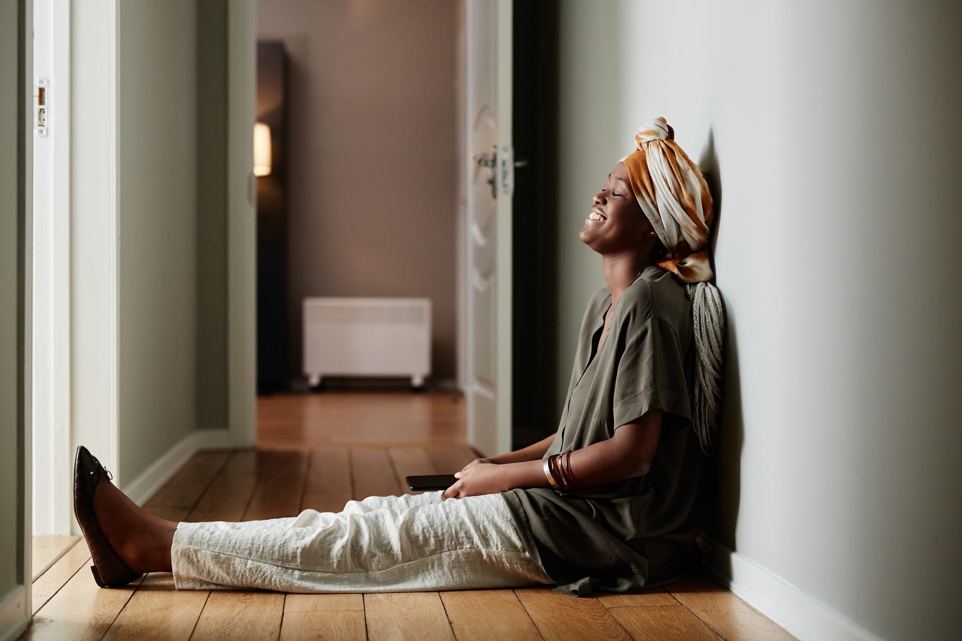 A woman is sitting on the floor leaning against a wall.