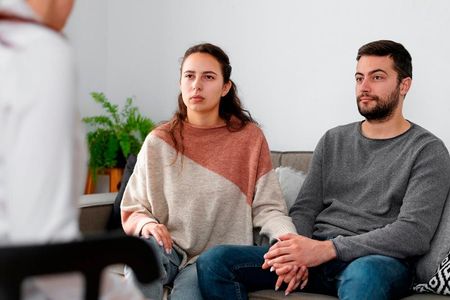 A man and a woman are sitting on a couch talking to a doctor.