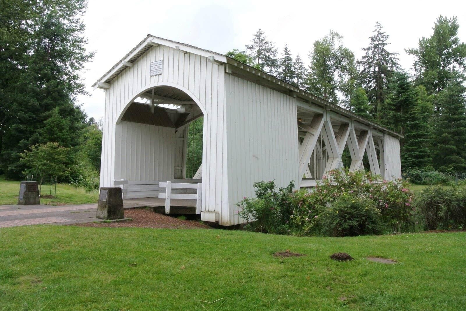 A white covered bridge in a park with trees in the background