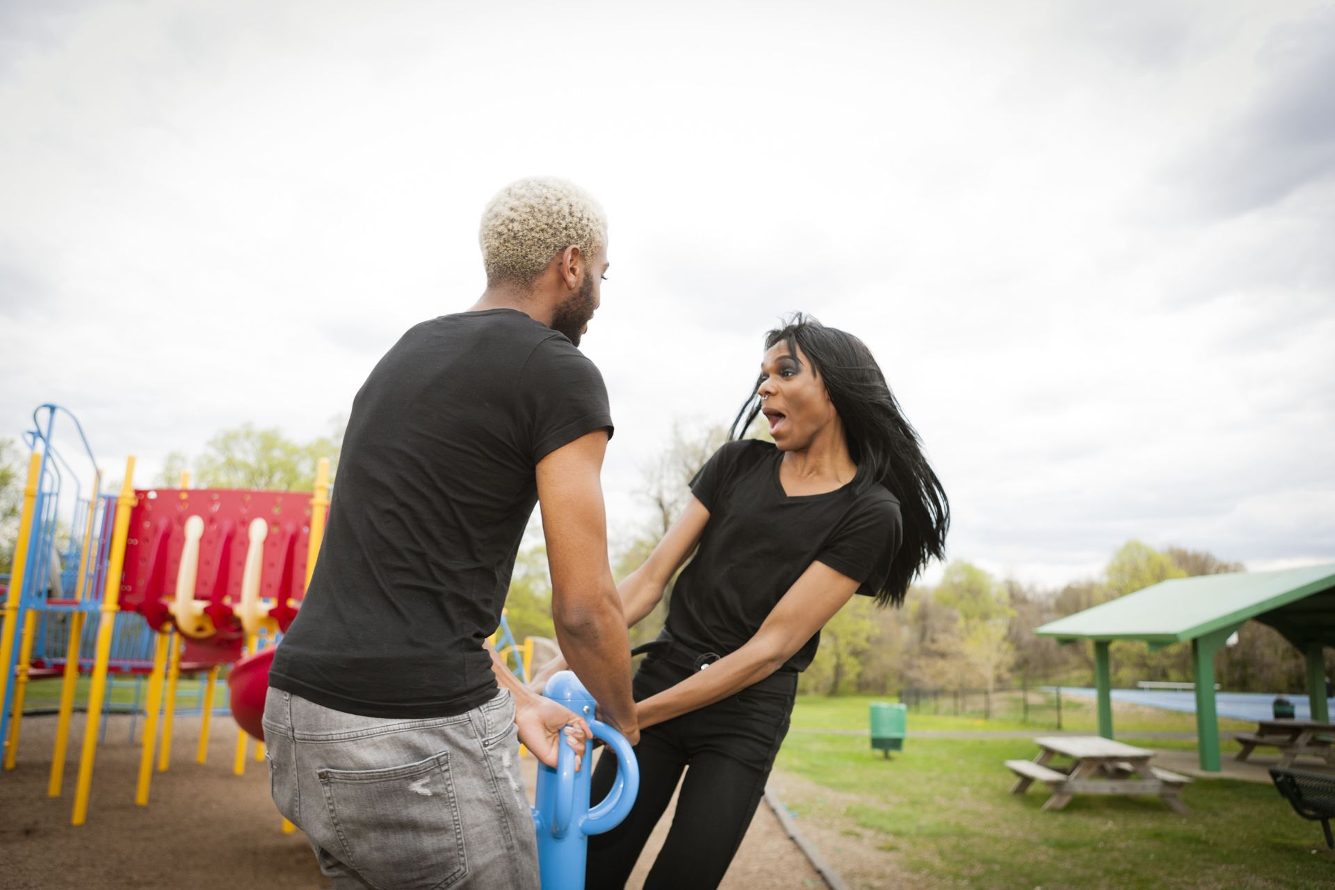 A man and a woman are playing on a seesaw in a park.