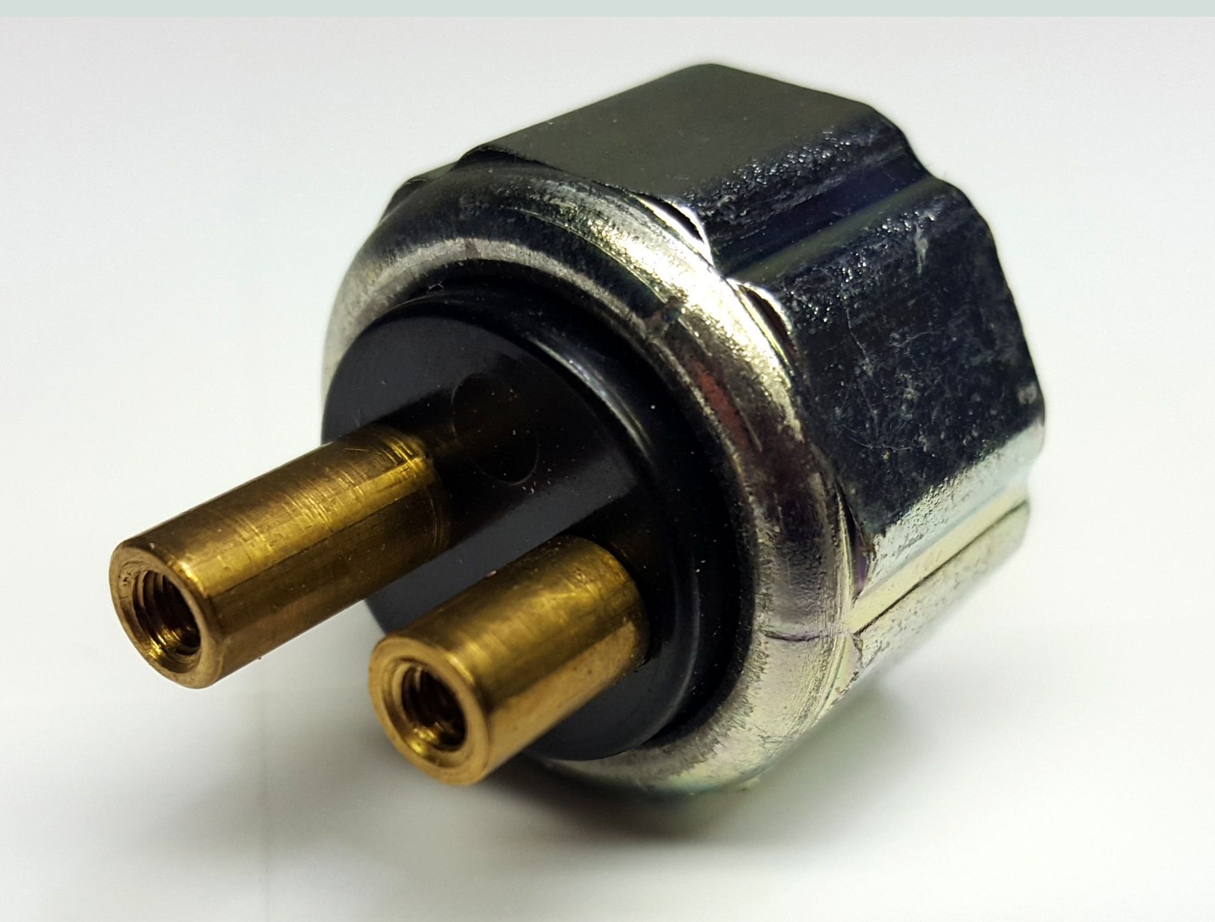 Two-pin electrical pressure sensor with a hexagonal metal body and brass terminals on a white background.