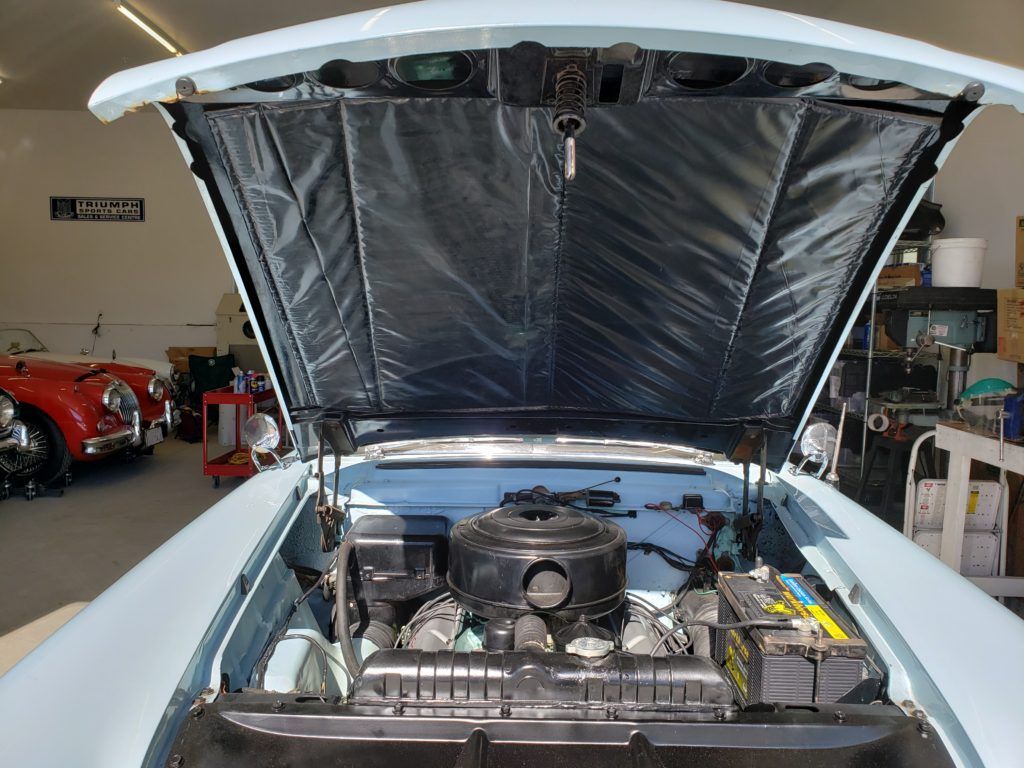 A vintage light blue car with its hood open, revealing the engine and a black padded interior.