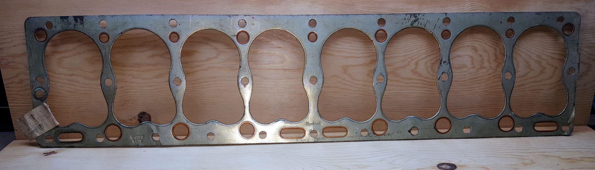 A metallic head gasket with eight oval-shaped holes, likely for an engine.