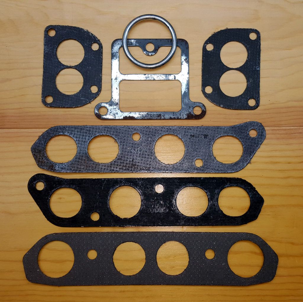 Gasket set on wood surface. Includes various black and silver gaskets with holes and a metal bracket.