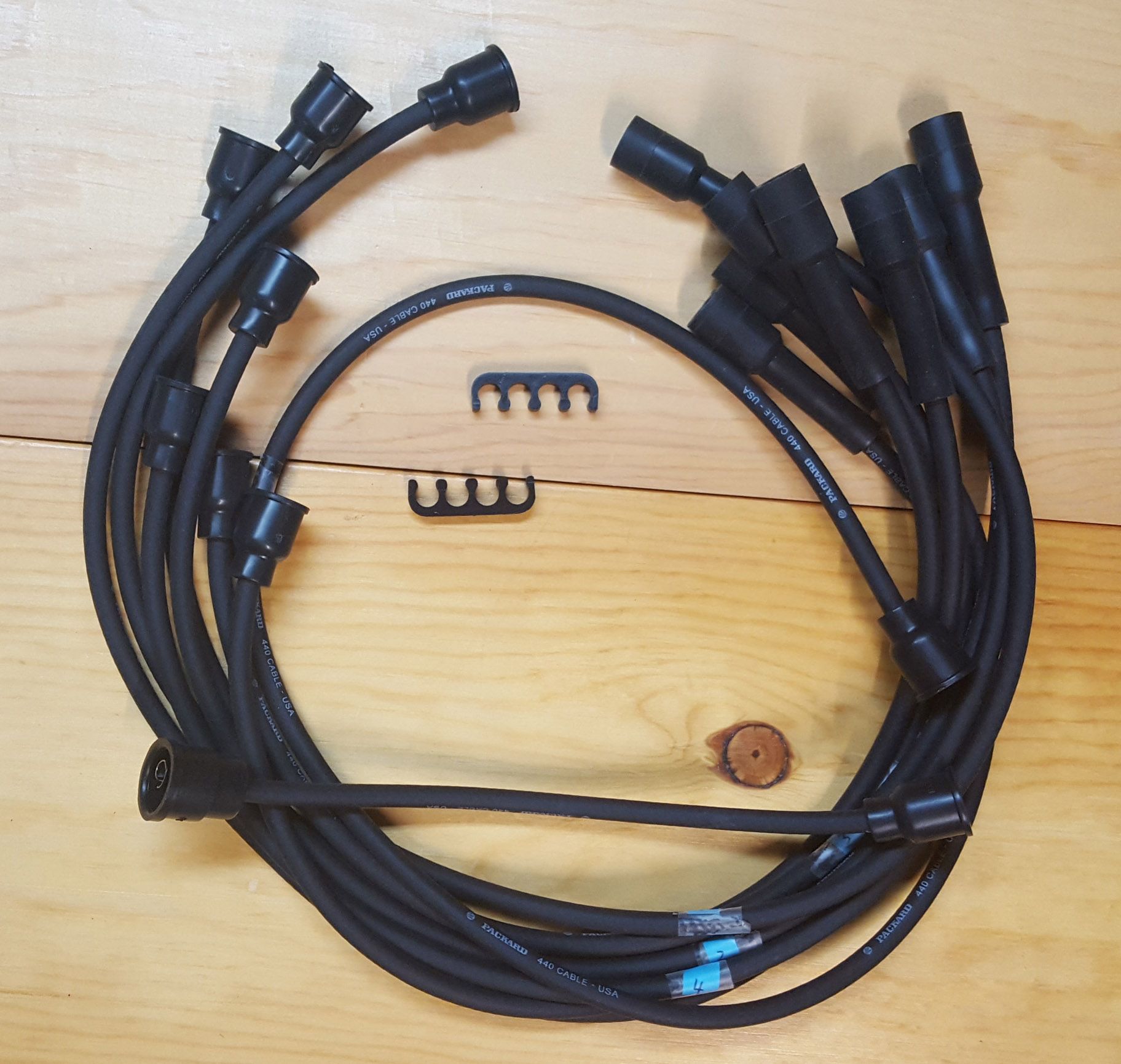 A set of black spark plug wires with wire separators and a brown component, resting on a wooden surface.