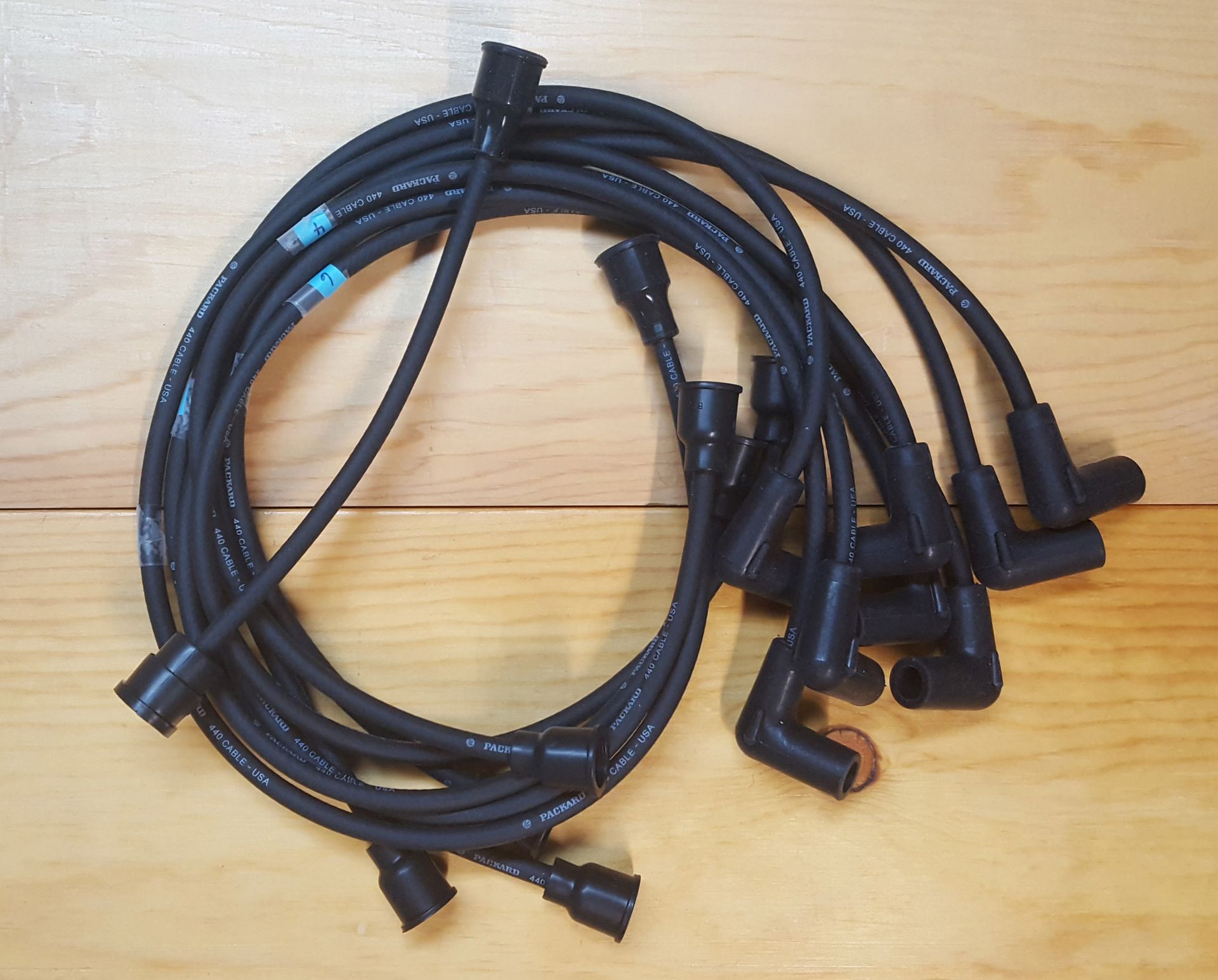 Black spark plug wires coiled on a wooden surface.