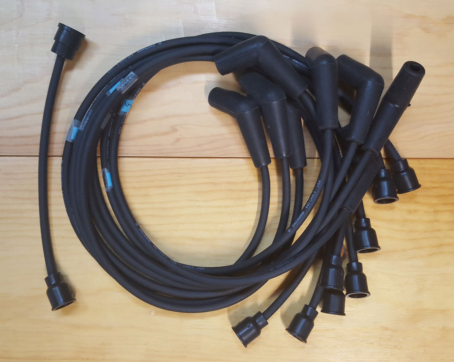 A set of black spark plug wires coiled on a light brown wooden surface.