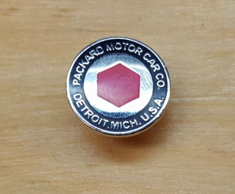 Round Packard Motor Car Co. emblem with a red hexagon in the center, set against a wooden surface.