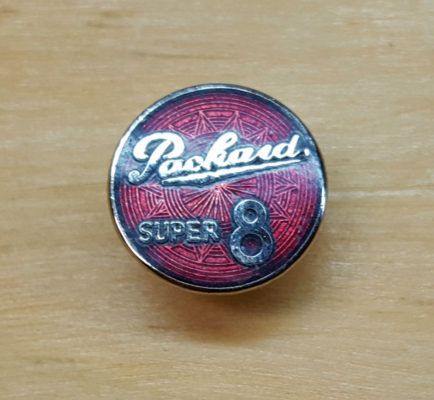 A red and silver Packard Super 8 emblem on a wooden surface. The logo features stylized lettering.