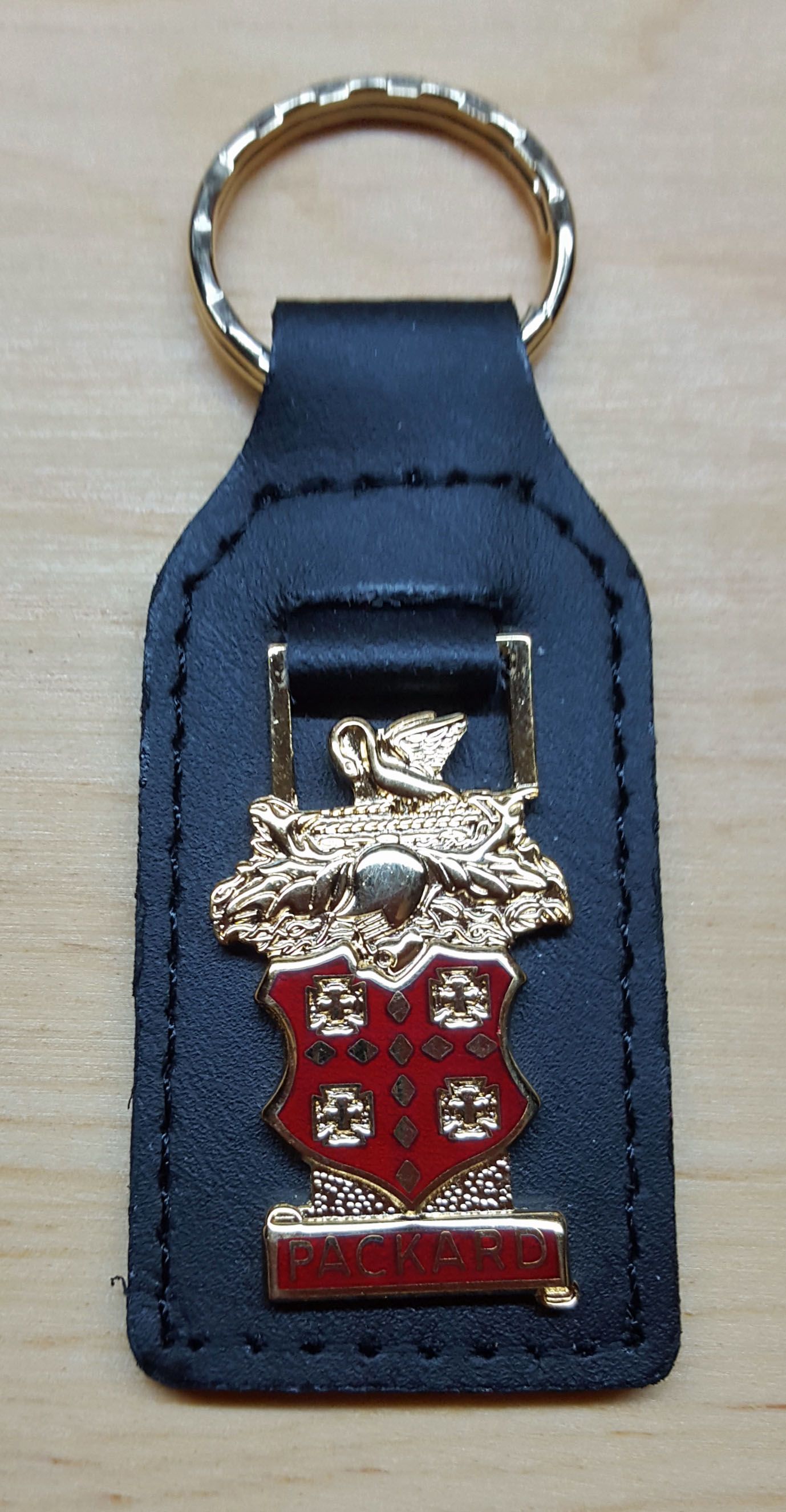 Black leather keychain with gold trim and ring. The decorative emblem has a red shield and gold embellishments.