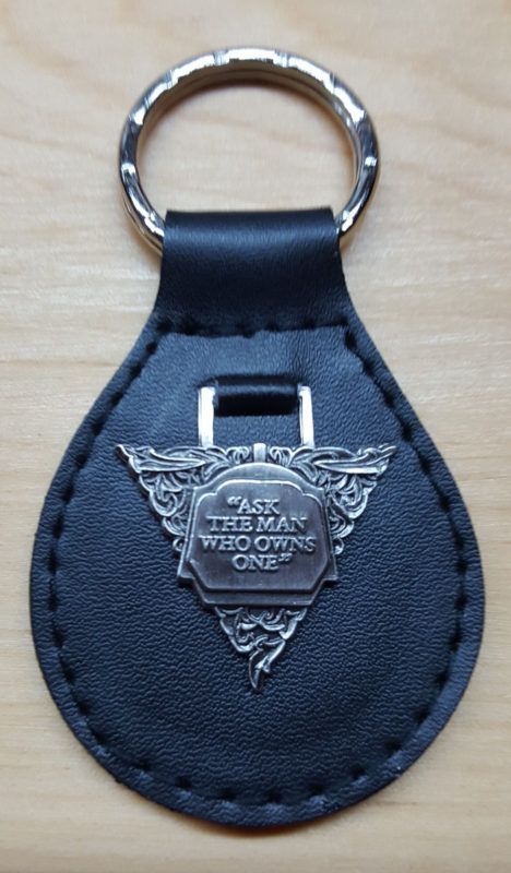 Black leather key fob with a silver ring. The fob has a decorative silver emblem with the text 