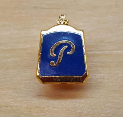 Gold-framed blue pin with a stylized gold 
