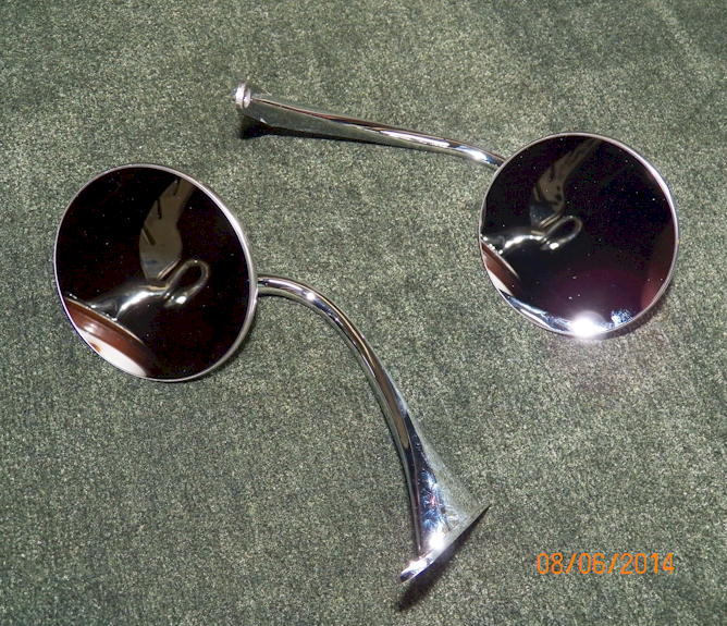 Two chrome side mirrors with circular reflective surfaces, resting on a dark green surface.
