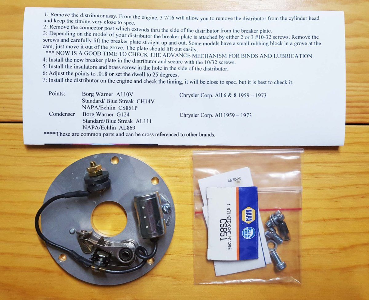 A vintage car ignition assembly with a bag of hardware and an instruction sheet on a wooden surface.