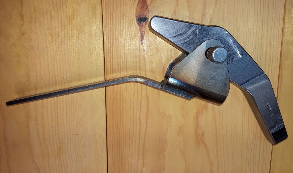 Metal latching mechanism with a long handle on a wooden surface. The mechanism is silver-colored, with a pivoting action.