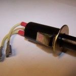 A black push-button switch with three wires, a mounting washer, and metal bracket.