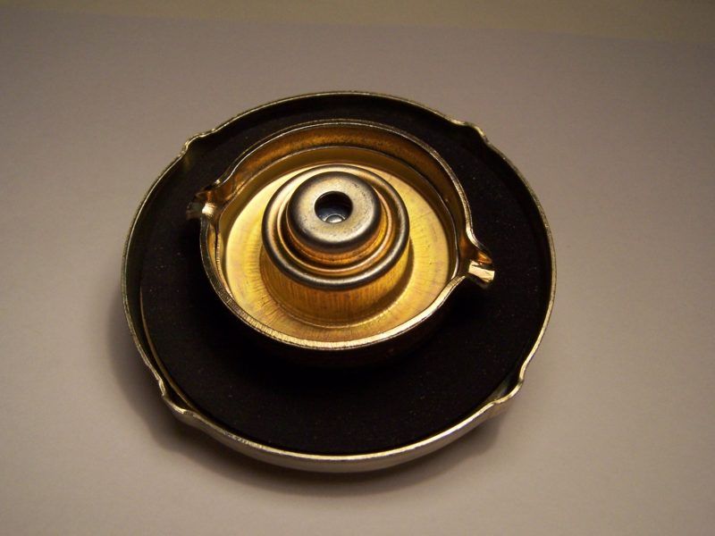 A gold and black fuel cap, likely for a car, with a metal interior and black rubber seal.