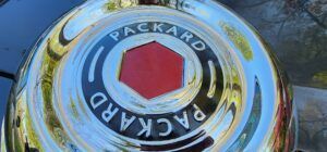 Chrome Packard emblem with the brand name in white lettering on a black background, over a red hexagon.