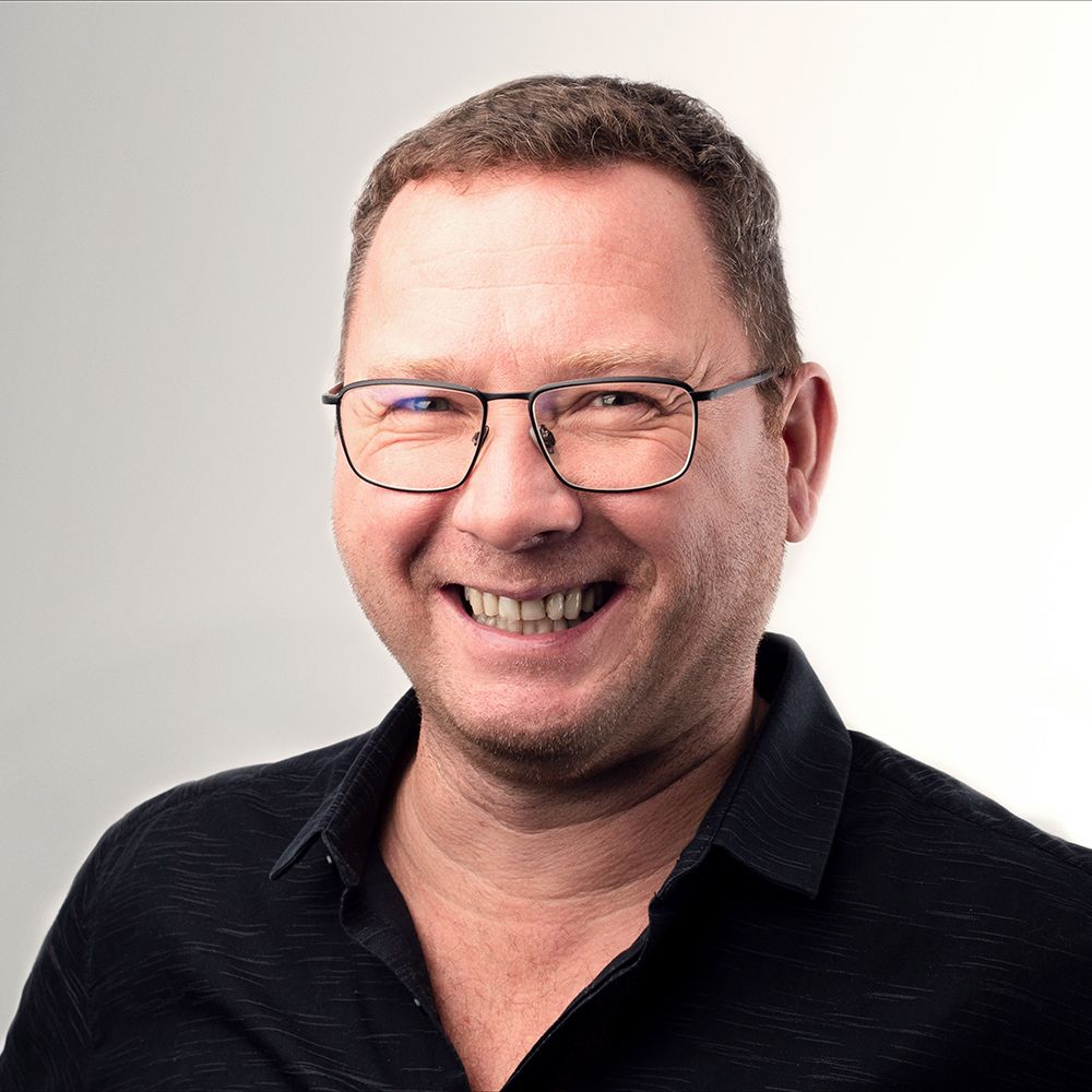 A man wearing glasses and a black shirt is smiling.