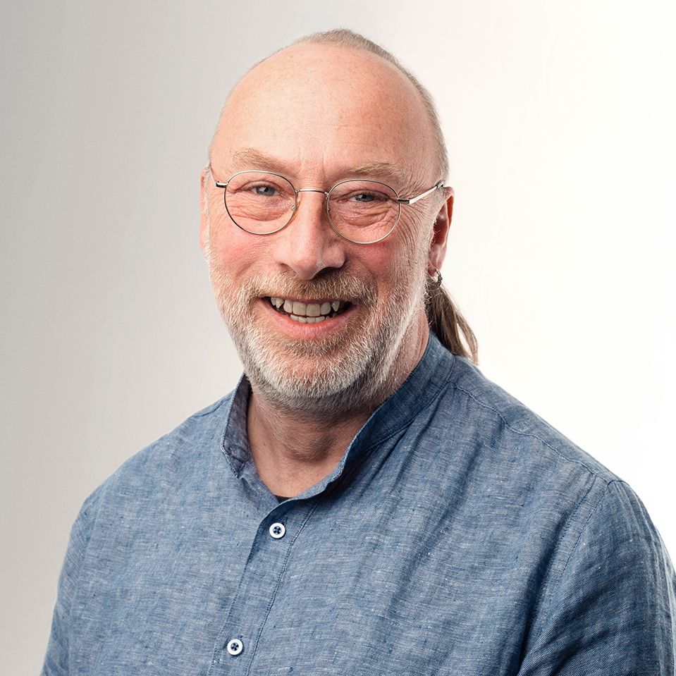 A man with a beard and glasses is wearing a blue shirt and smiling.
