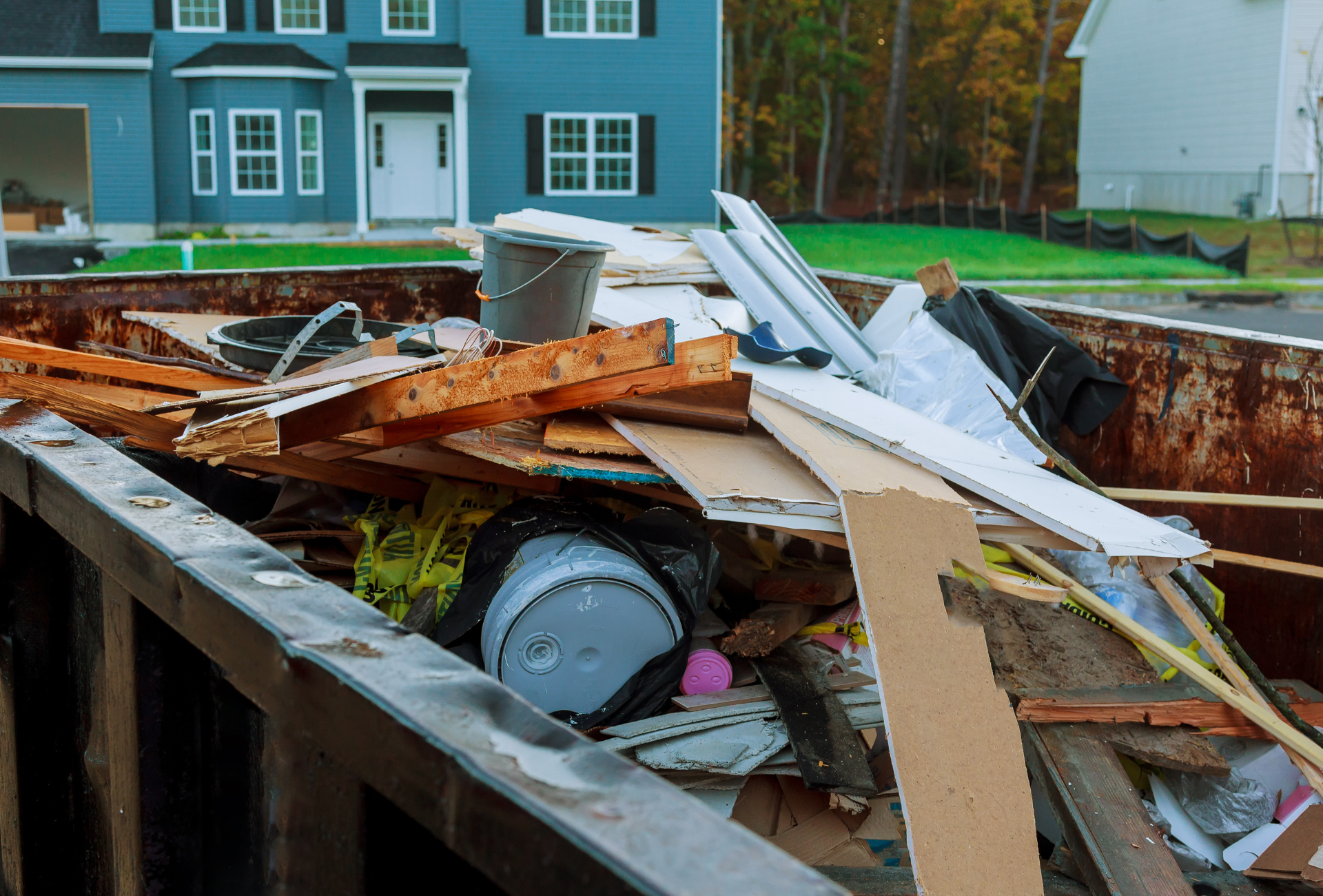 A dumpster filled with junk in front of a blue house.