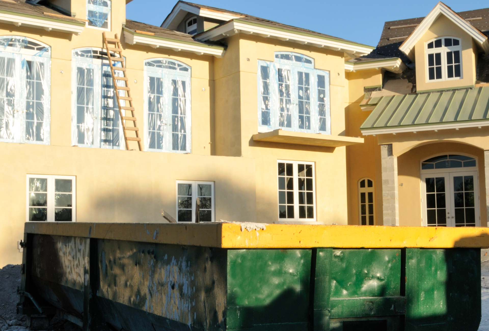 A large yellow house with a green dumpster in front of it