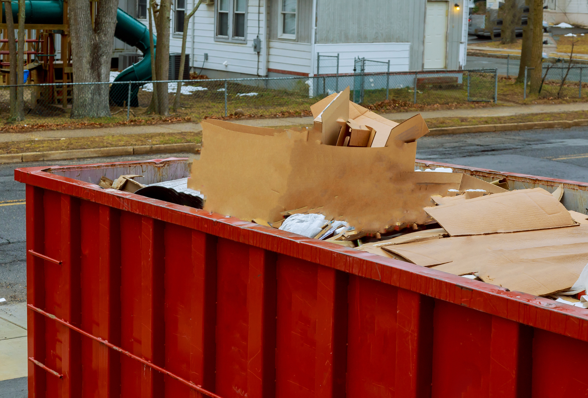 A red dumpster filled with cardboard boxes in a parking lot