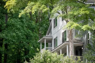 A white house with a porch is surrounded by trees.