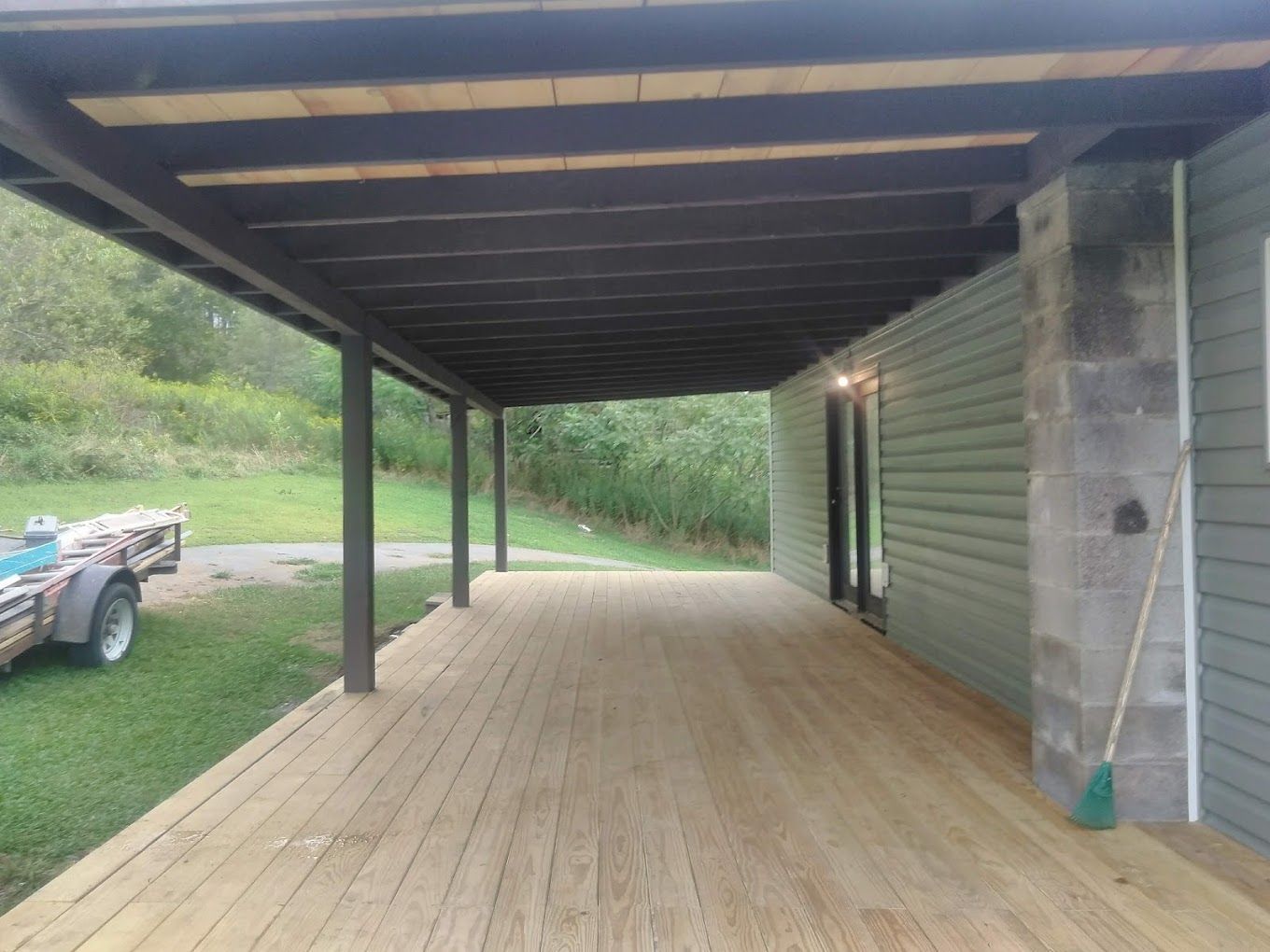 A wooden deck with a broom and a trailer parked underneath it.