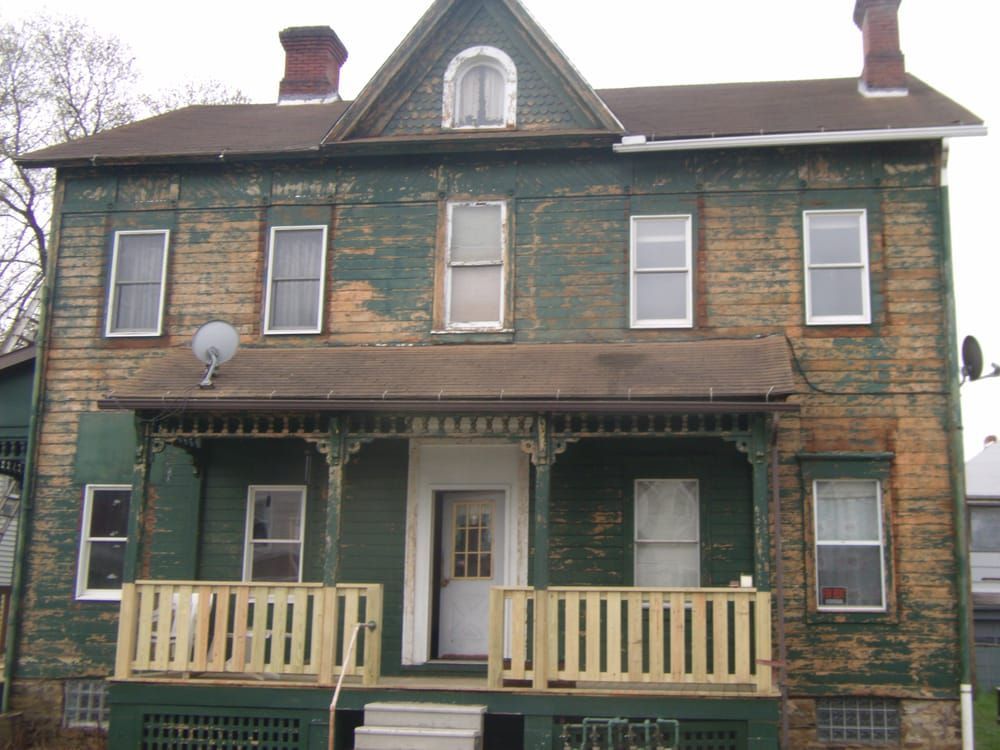 A green house with a porch and a satellite dish on the roof