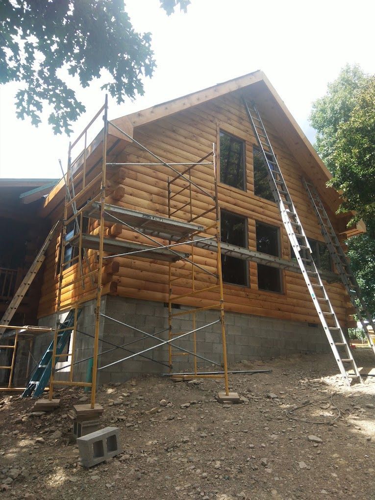 A log cabin is being built with scaffolding and a ladder.