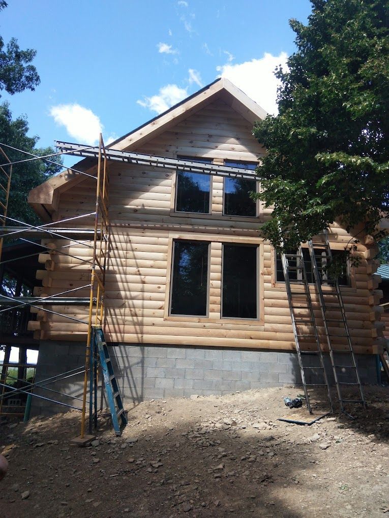 A log cabin is being built with a ladder in front of it