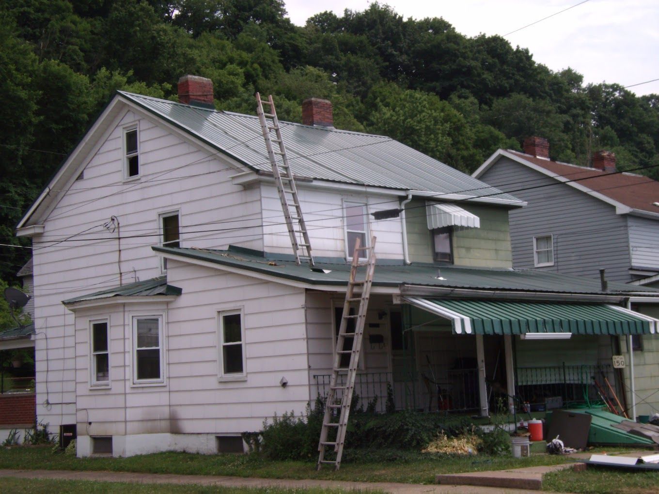 A white house with a green awning and a ladder on the roof