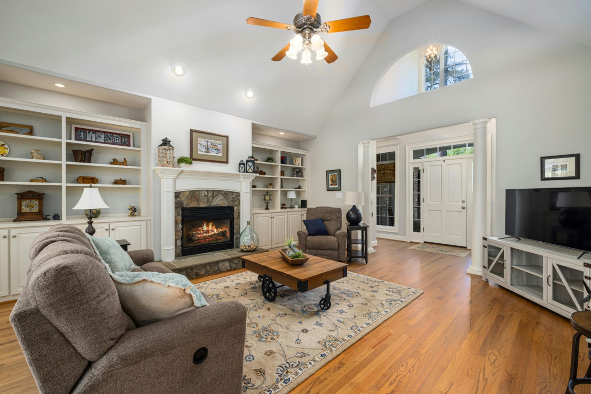 Living room with fireplace, built-in shelving, brown sofa, rug, and hardwood floor.