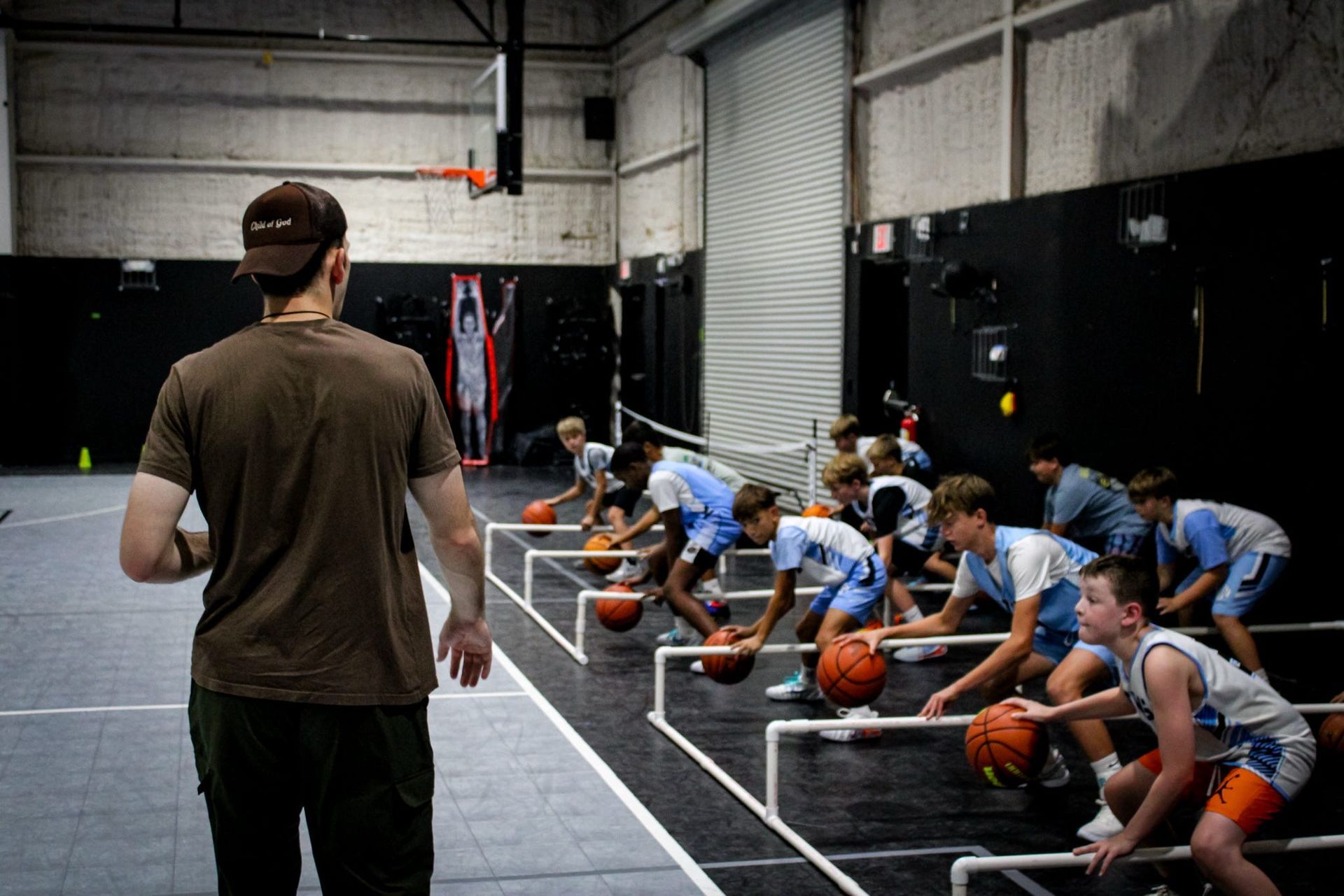 Coach observes basketball players practicing dribbling drills. Indoor gym setting.