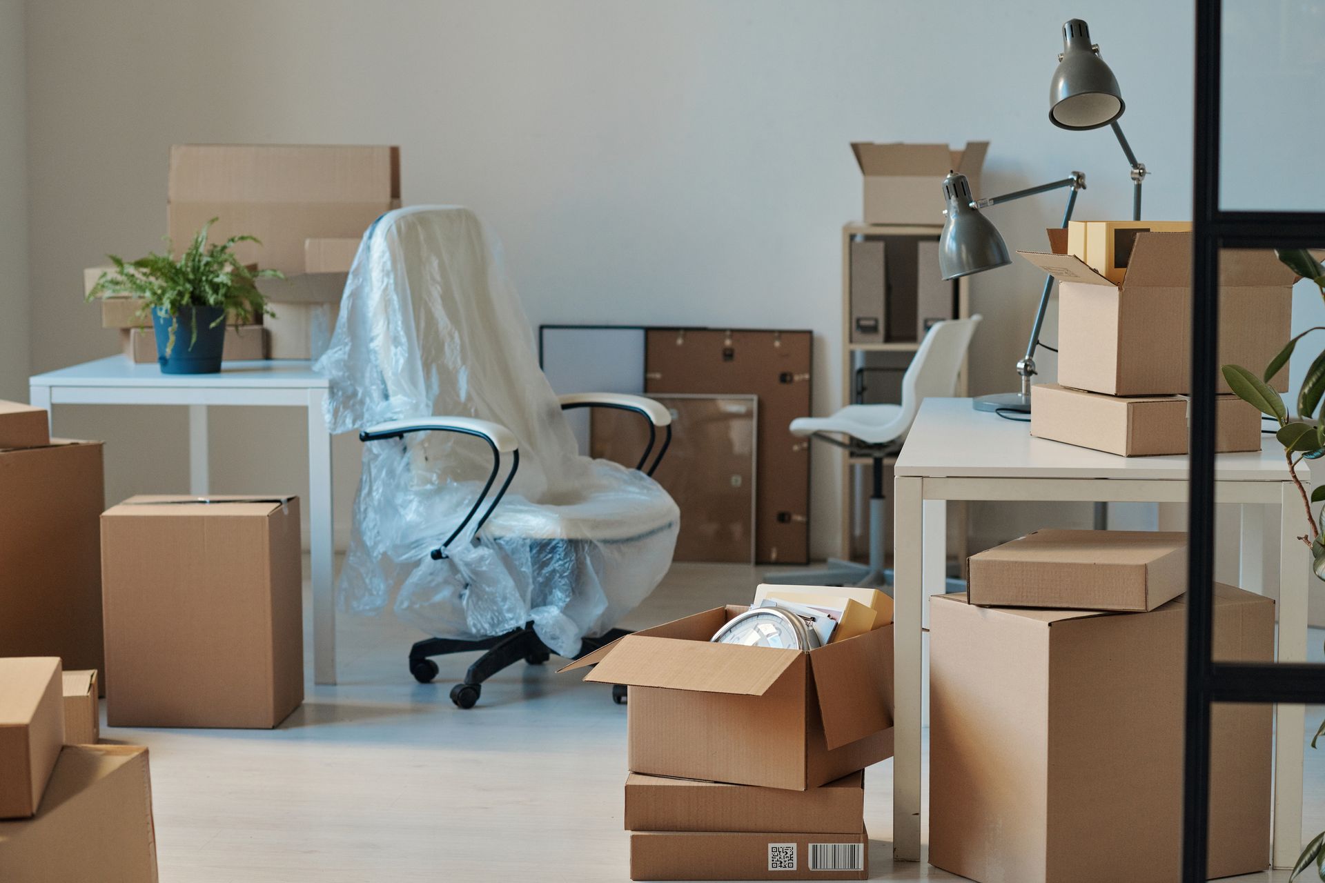 Office being moved; boxes stacked, chair covered in plastic, desks visible.