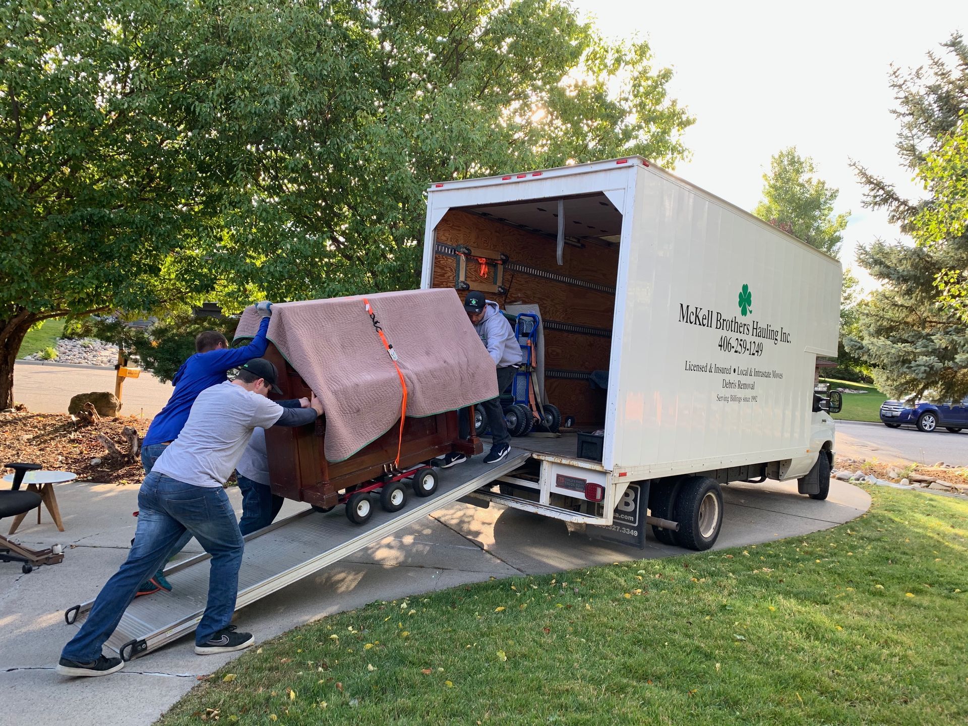 Two men loading a wooden cabinet into a moving truck on a ramp in a residential area.