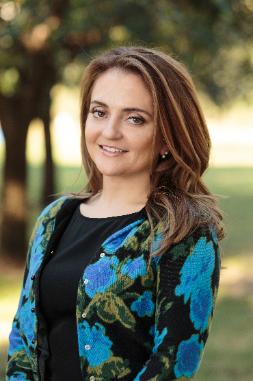 A woman wearing a black dress and a blue floral cardigan is smiling for the camera.