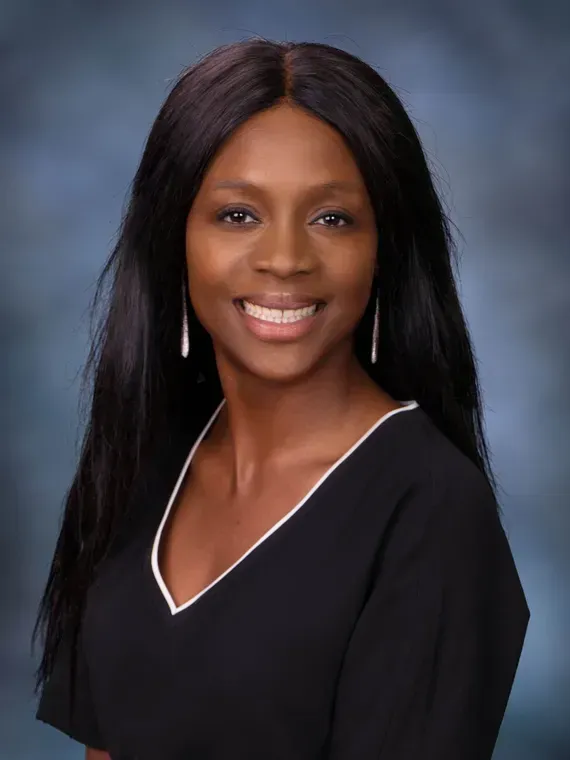 Woman with long black hair smiles, wearing a black top with white trim, against a blue backdrop.