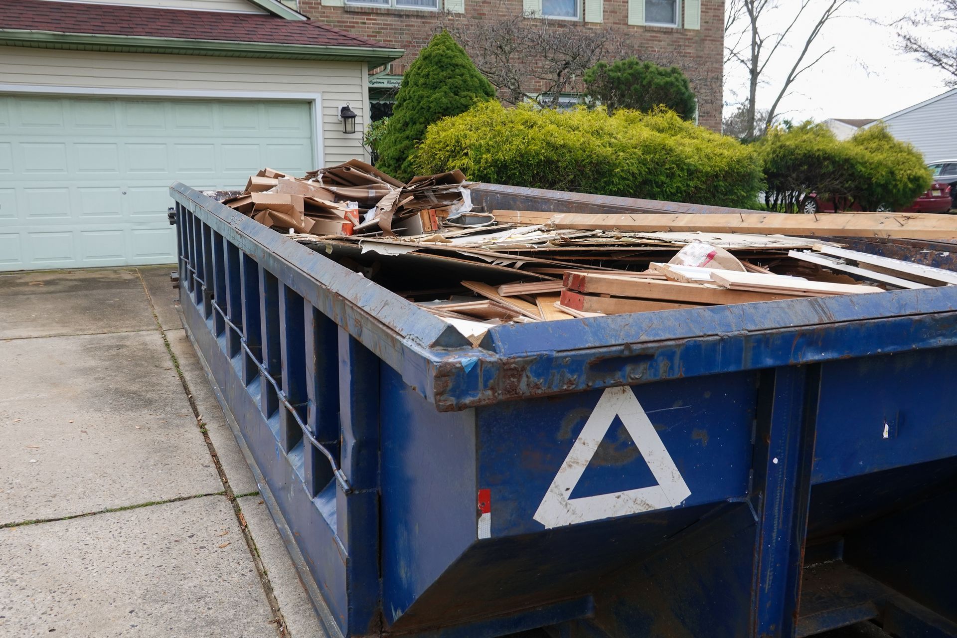 Red construction dumpster on a brick street beside a building with white-framed windows and doors