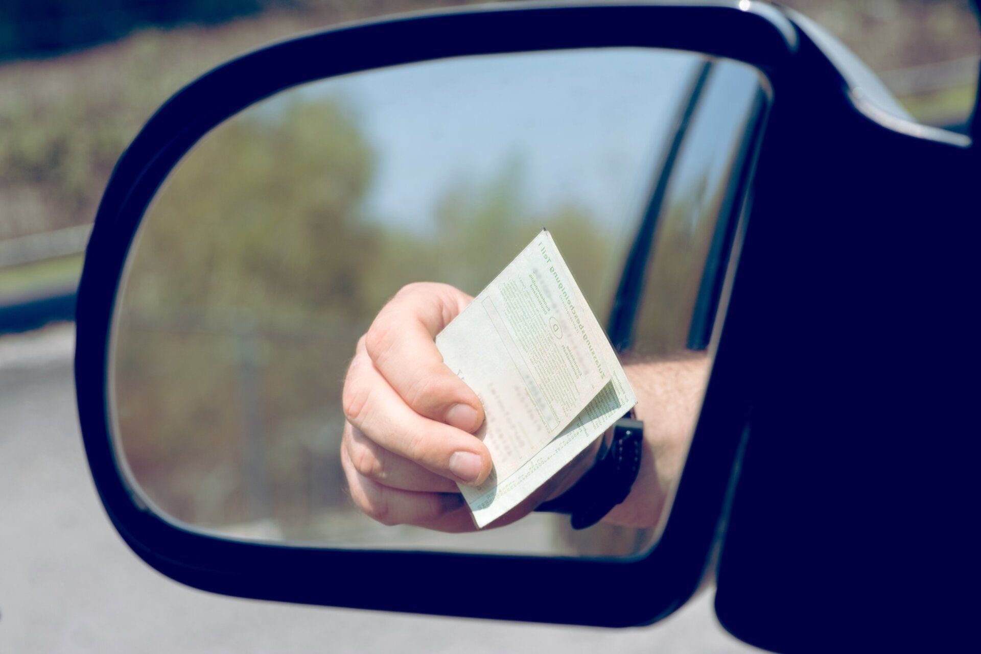 A person is holding a piece of paper in front of a car rear view mirror.