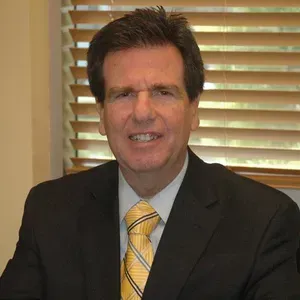 A man in a suit and tie is sitting in front of a window.