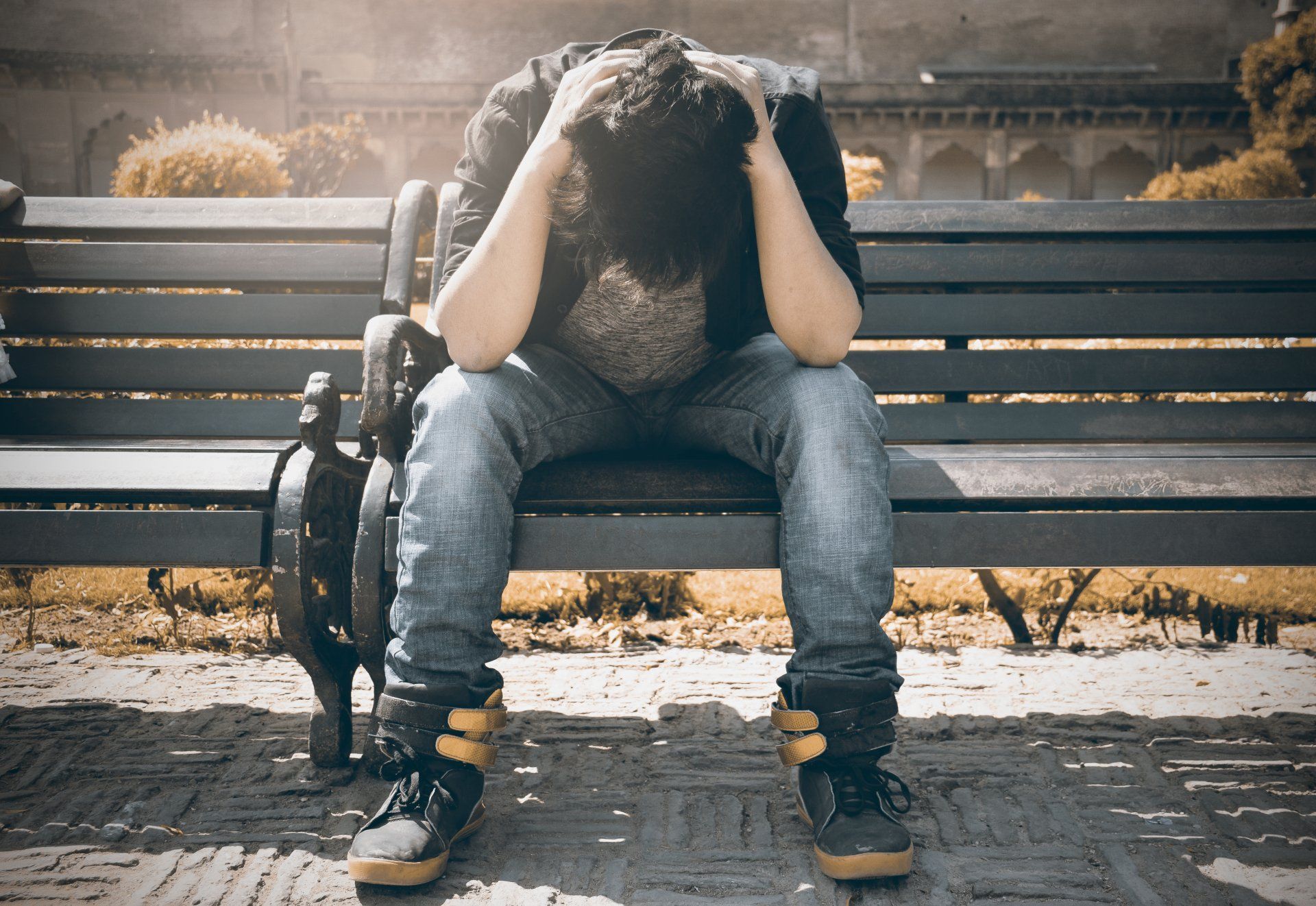 A man is sitting on a park bench with his head in his hands