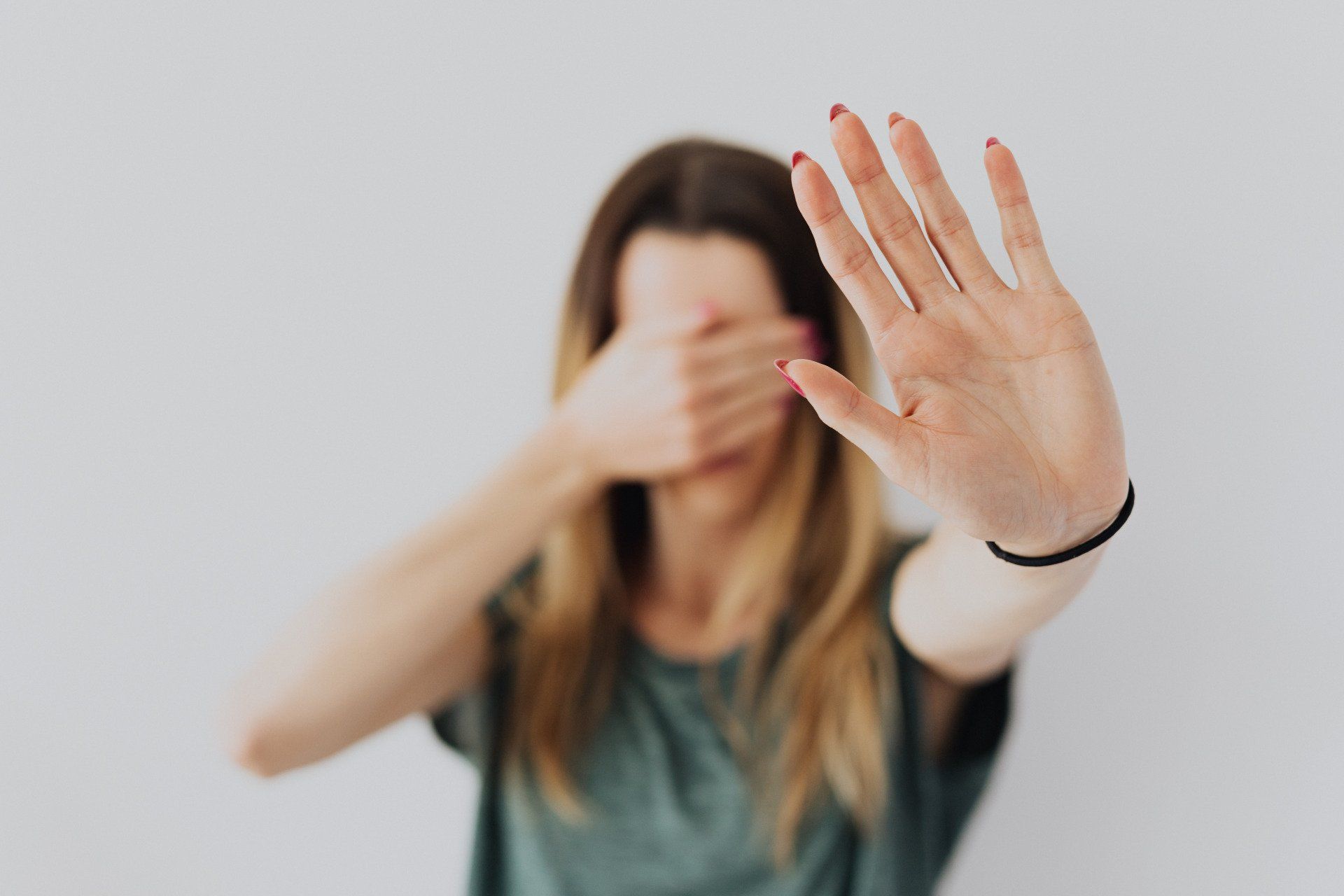 A woman is covering her face with her hand and making a stop sign.